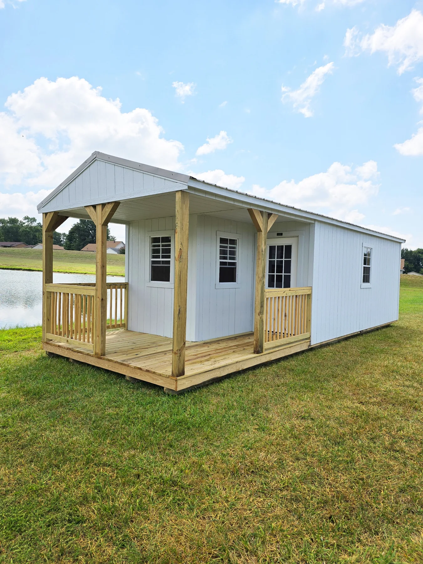 White Premier cabin shell with a wood porch beside a pond